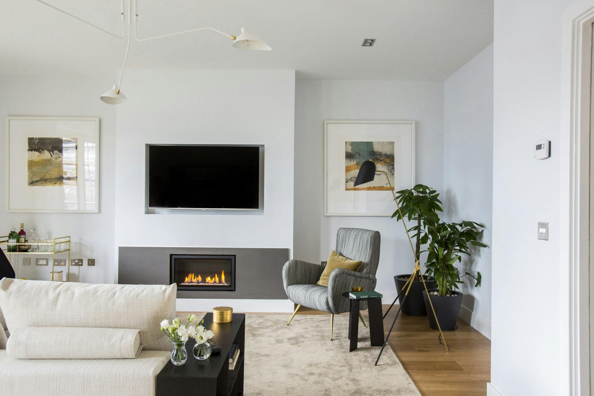 Modern living room with a wall-mounted TV, electric fireplace, abstract art, and a comfortable grey armchair.