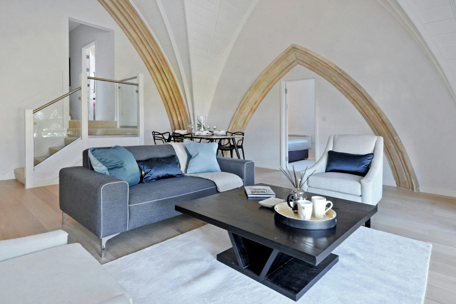 Spacious living room with vaulted ceilings, a grey sofa, white armchair, and a wooden arch leading to another room.