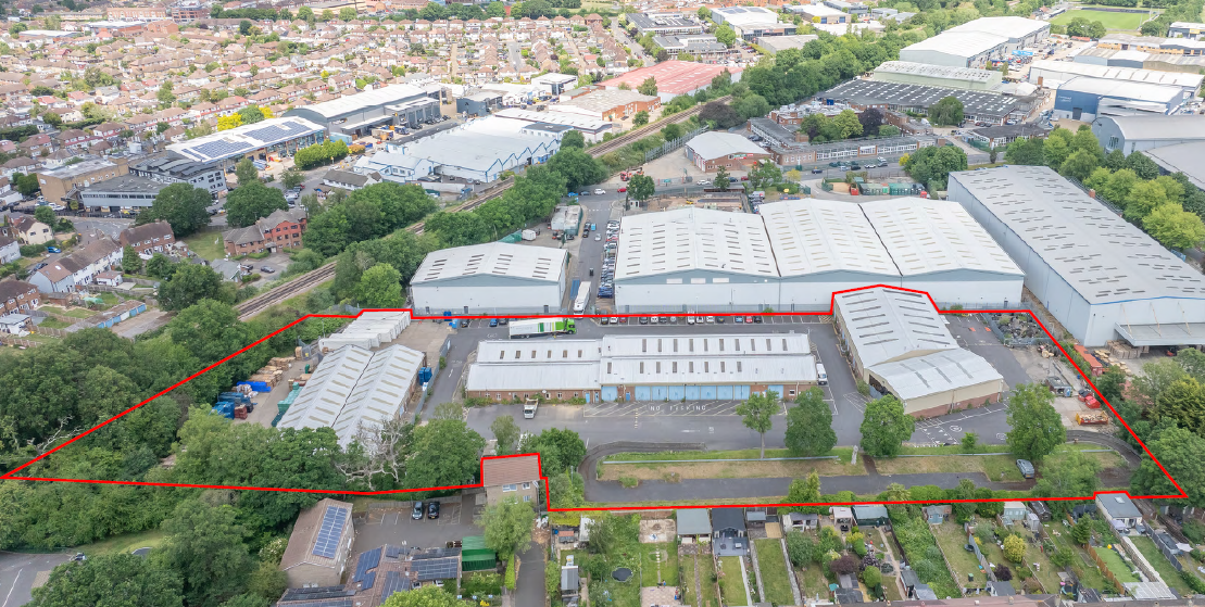 Aerial view of industrial complex with large white warehouse buildings outlined in red boundary, surrounded by residential areas and greenery.