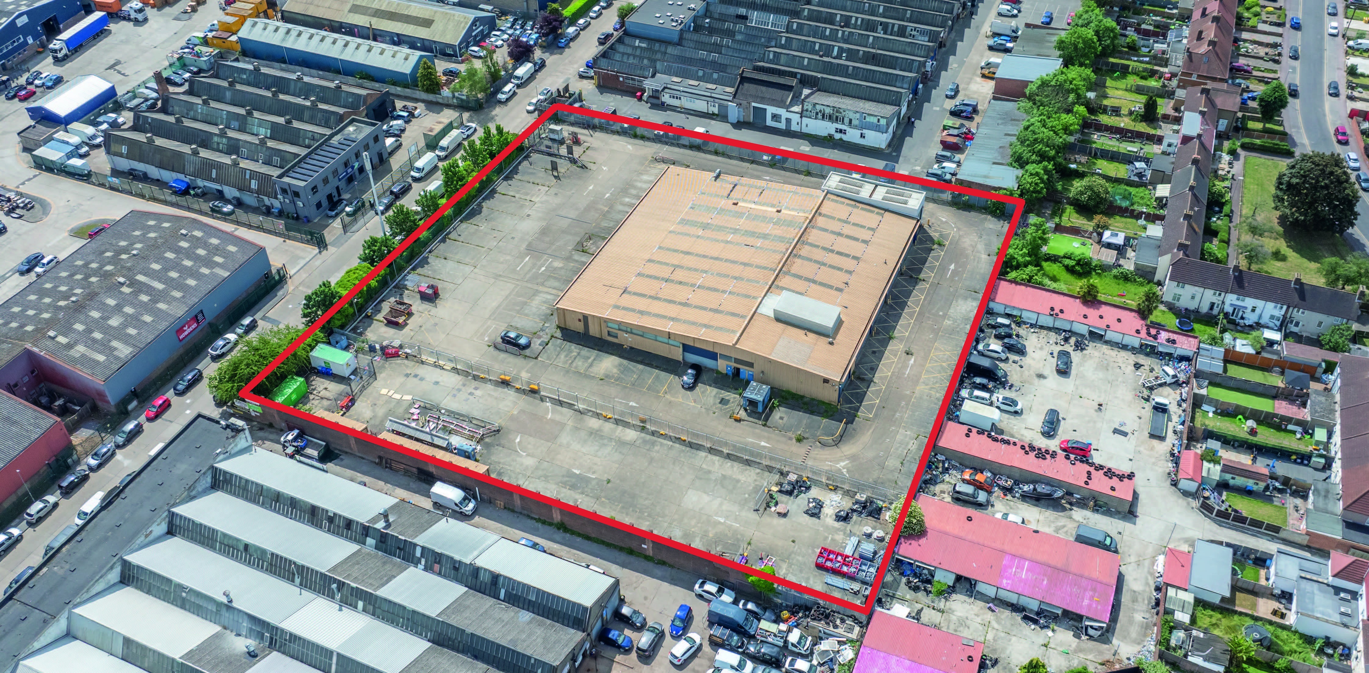 Aerial view of industrial area with large beige warehouse building outlined in red boundary, surrounded by grey buildings, car parks, and roads.