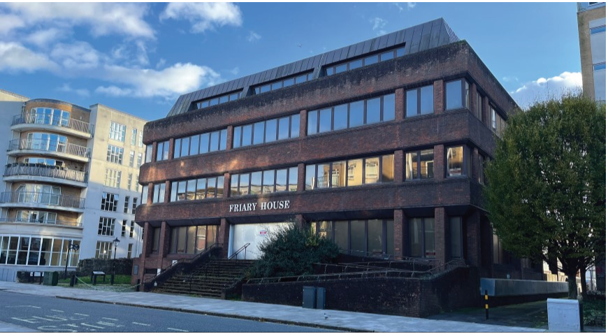 Exterior of Friary House, a multi-story brick office building with large windows, situated on a street with modern residential buildings nearby.