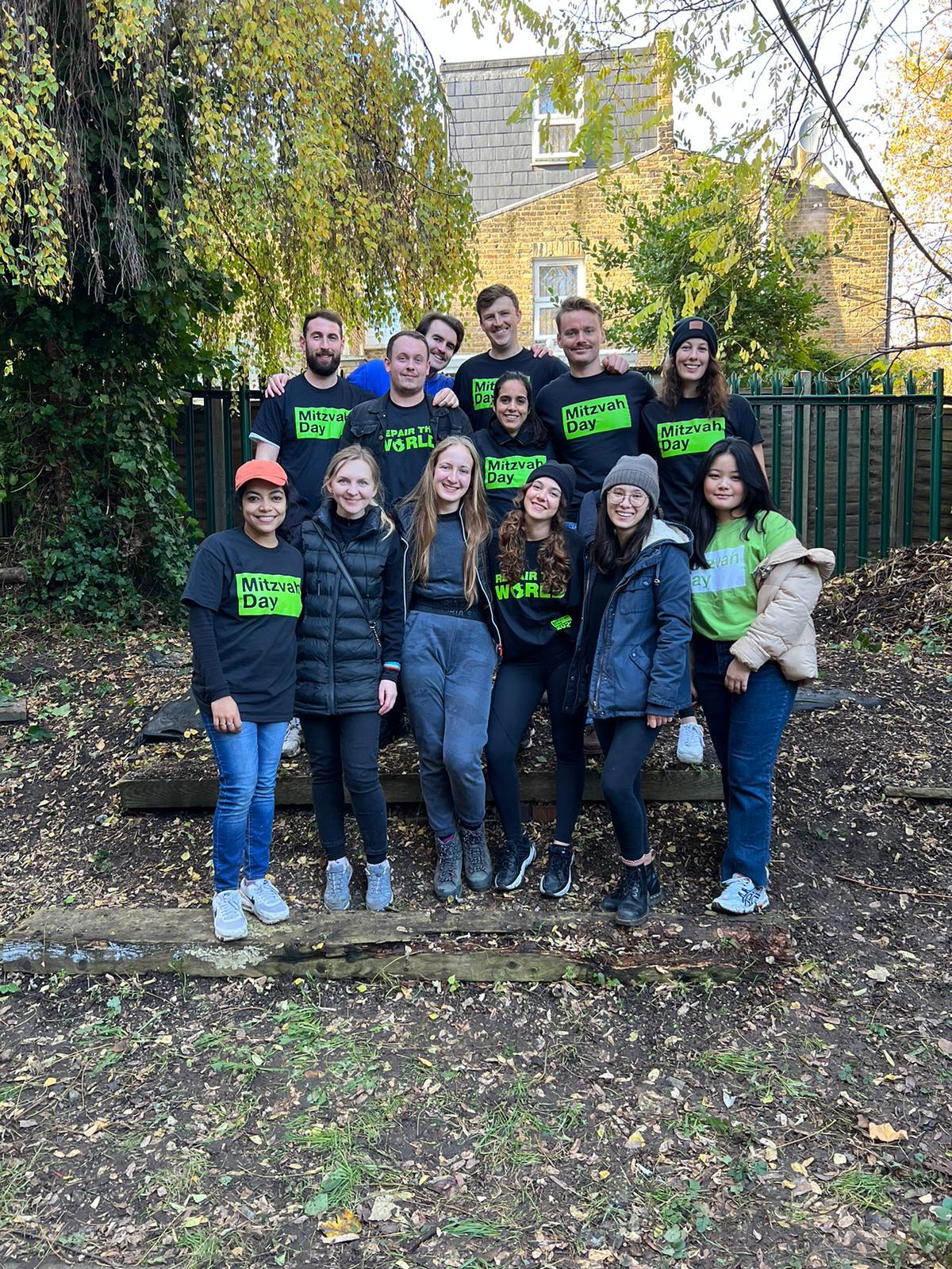 Group of people standing outdoors in a garden, some wearing matching green and black 'Mission Day' shirts, smiling for a group photo.