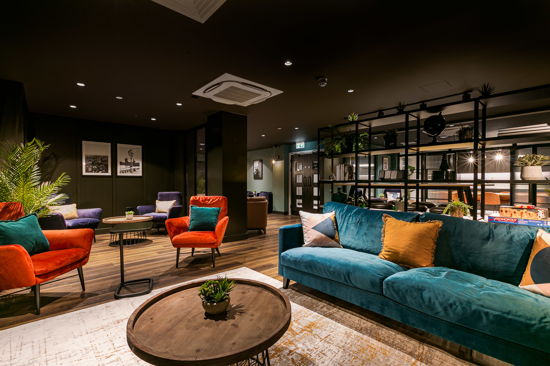 Chic lounge area with velvet sofas, ambient lighting, shelf decor, and a warm, inviting colour scheme.