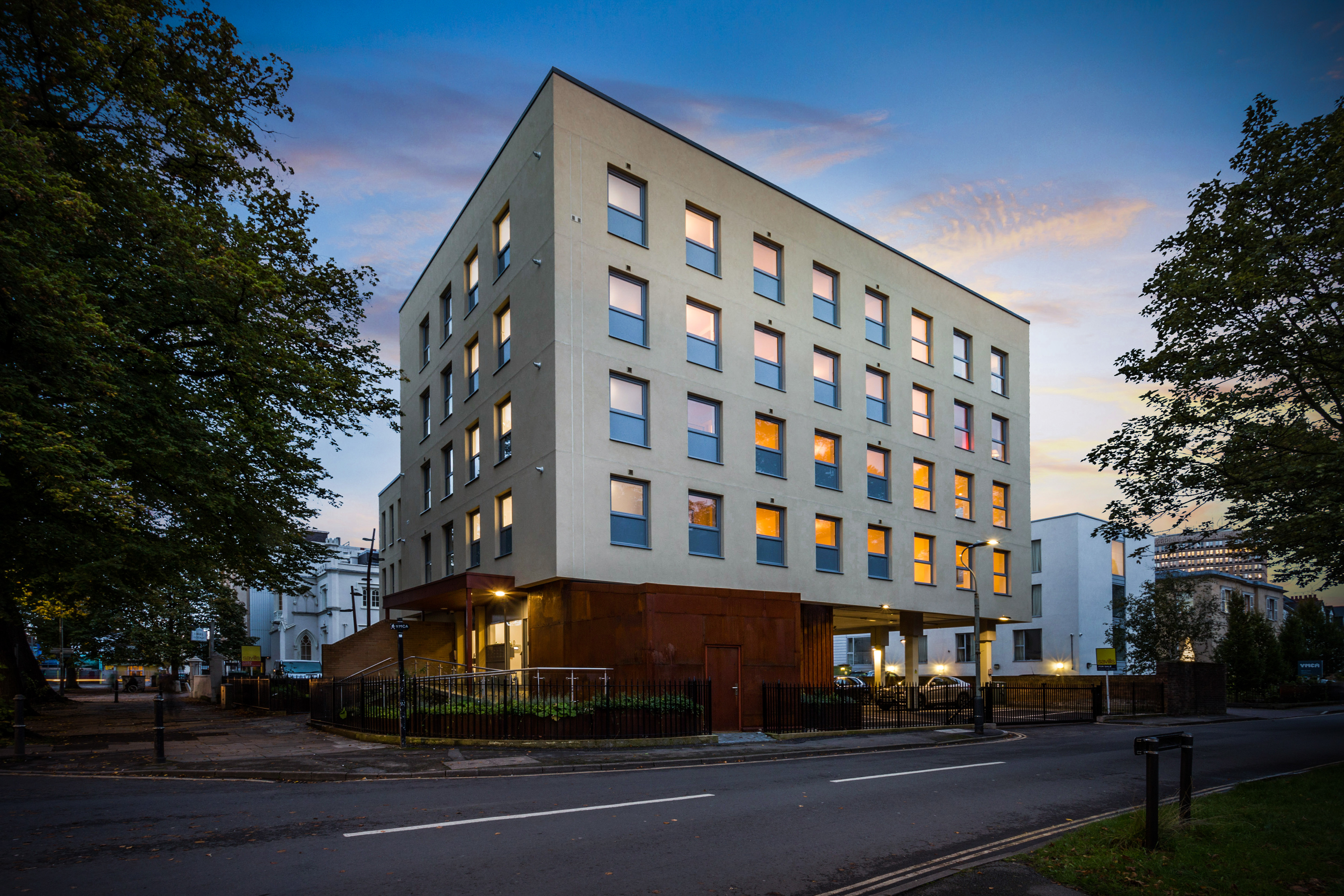 A contemporary multi-storey building at dusk with illuminated windows, set against a twilight sky.
