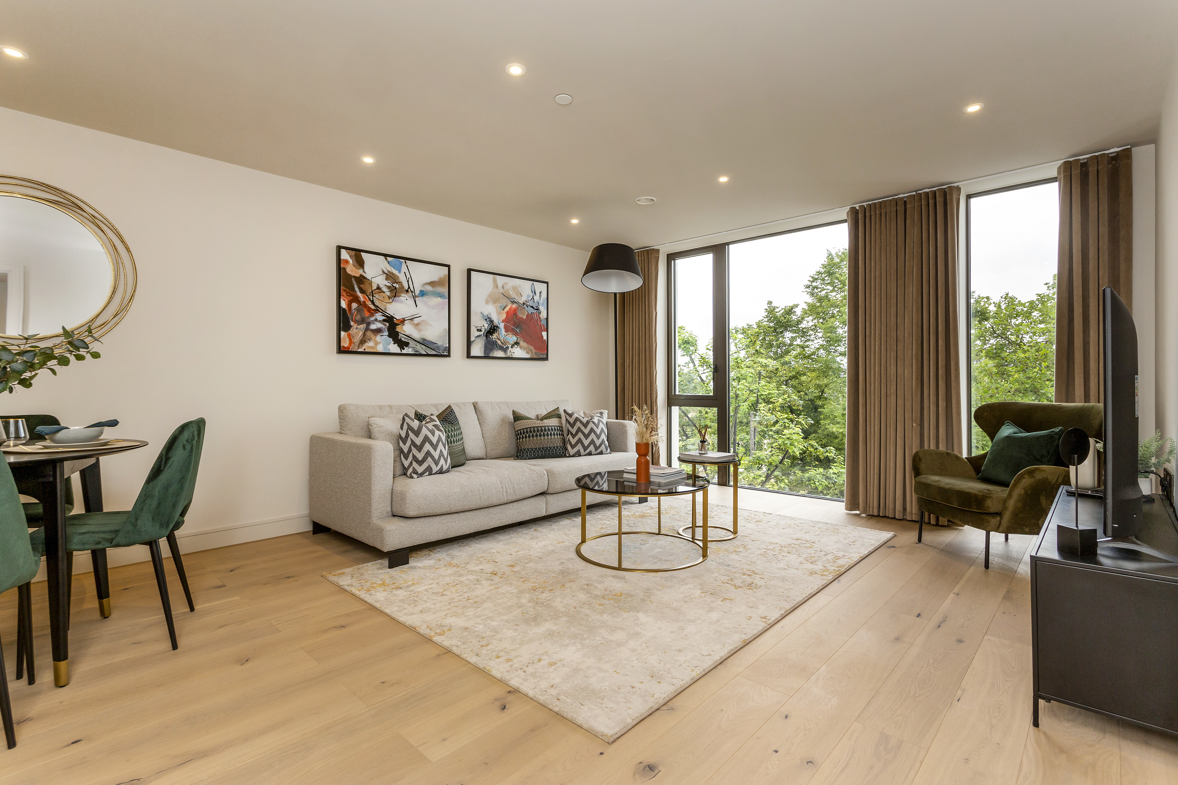 Stylish living room with a grey sofa, abstract wall art, large windows with a view of trees, and modern furnishings.