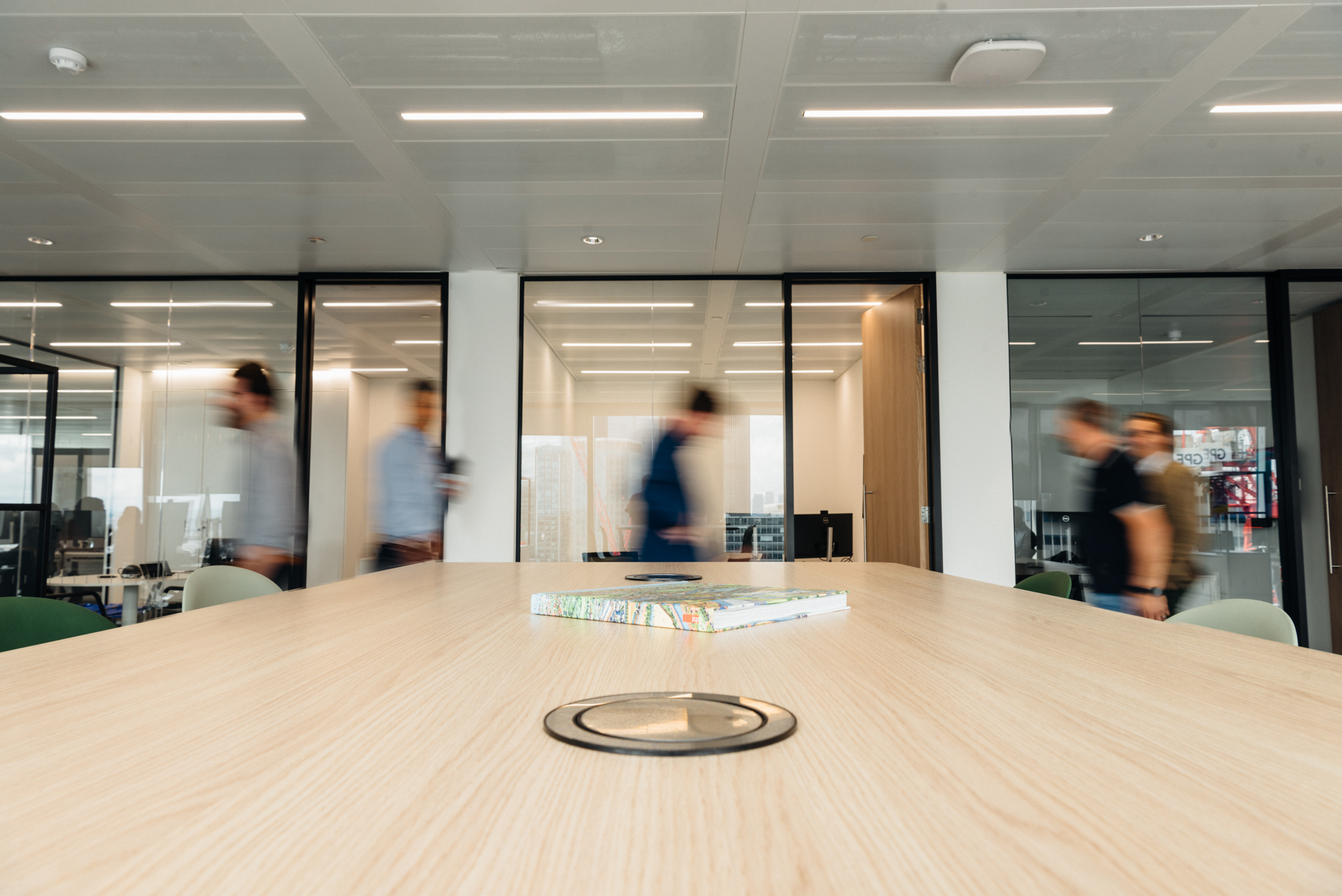 Blurred motion of people walking past a long conference table in a modern office setting