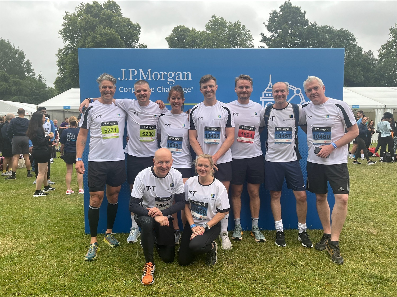 Group of runners posing together in front of a J.P. Morgan Corporate Challenge sign, wearing race bibs and matching athletic attire.