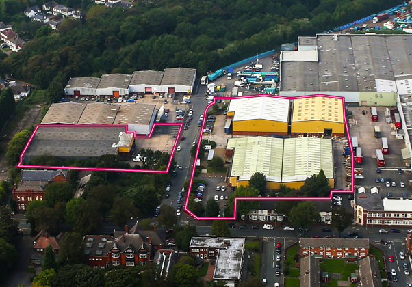 Aerial view of an industrial estate with several buildings, two of which are outlined in pink, surrounded by trees and residential areas.