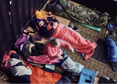 People in sleeping bags lying on the ground outdoors, participating in a sleep-out event.