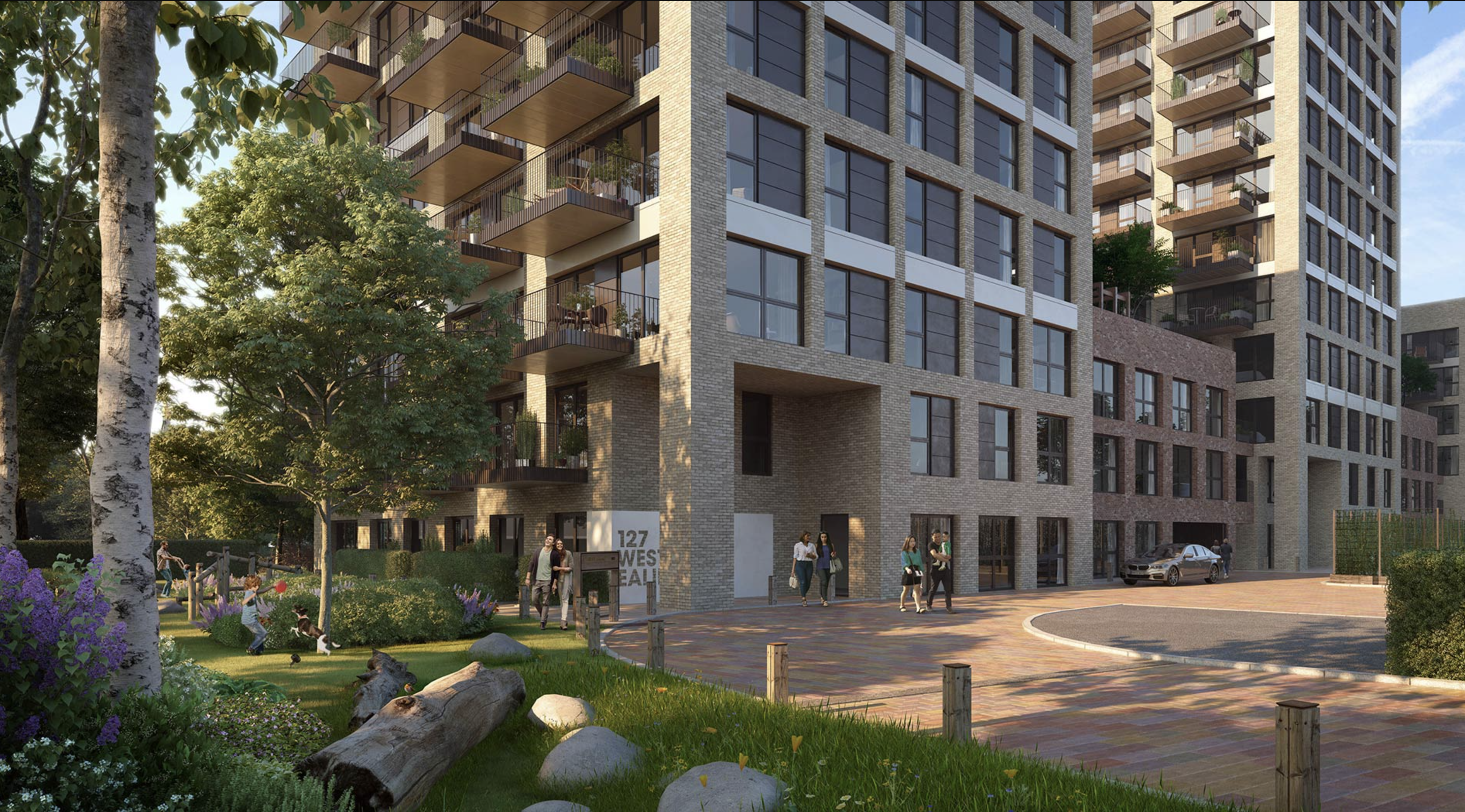A modern apartment building with large windows and balconies, surrounded by landscaped gardens. People are walking near the entrance, labelled '127', and cars are parked near the curved driveway. The garden features trees, flowers, rocks, and wooden logs for decorative seating.