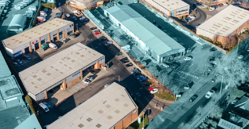 Aerial view of an industrial and commercial complex with several warehouse-style buildings and parking areas, located at a road intersection.