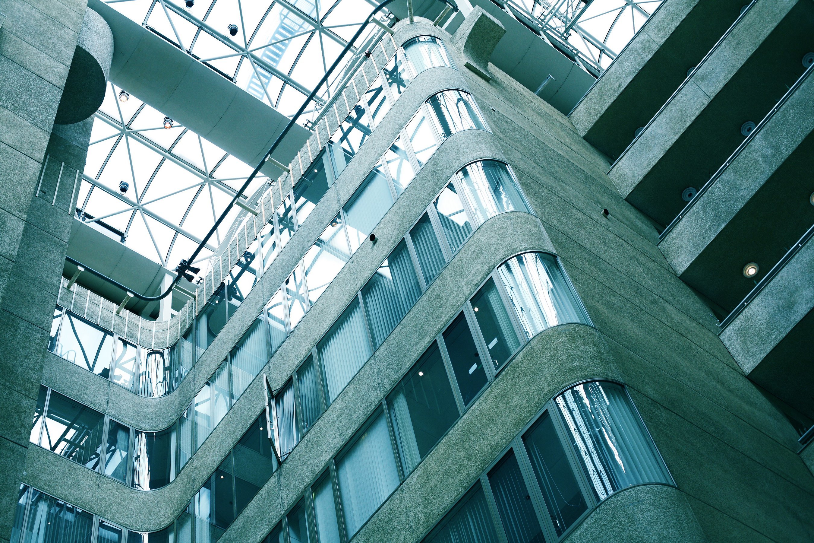 Upward view of a modern building interior with curved concrete balconies, large windows, and a glass ceiling.