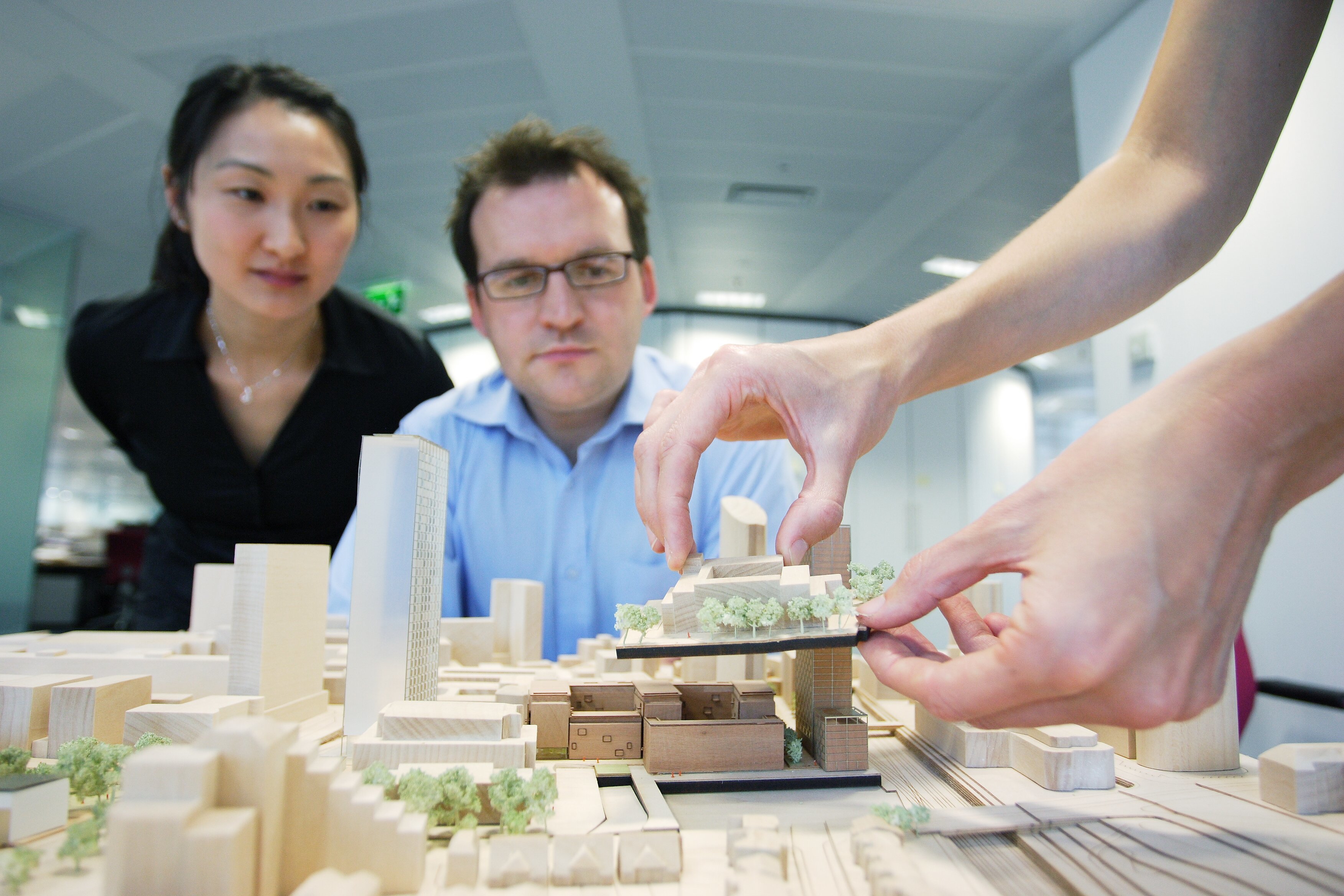 Two people observing a detailed architectural model while a third person adjusts a part of the structure.