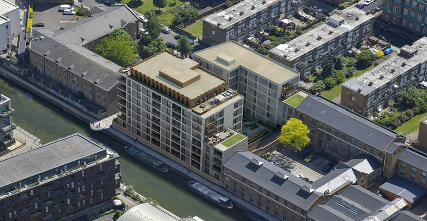 "Aerial view of a modern multi-story residential building complex situated along a canal, surrounded by other buildings in an urban neighborhood.